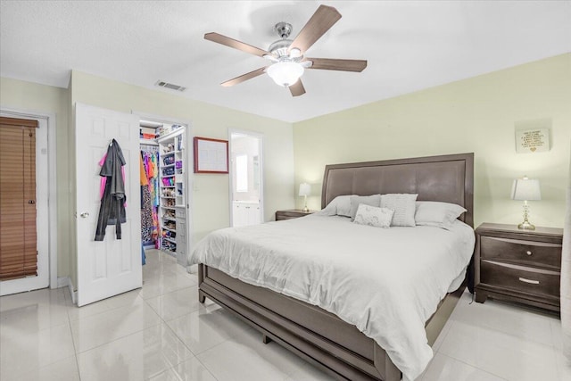 bedroom with ensuite bathroom, a walk in closet, ceiling fan, light tile patterned floors, and a closet