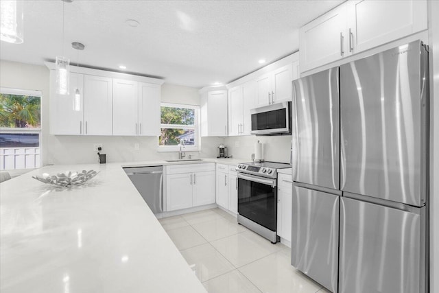 kitchen featuring white cabinetry, sink, stainless steel appliances, decorative light fixtures, and light tile patterned flooring