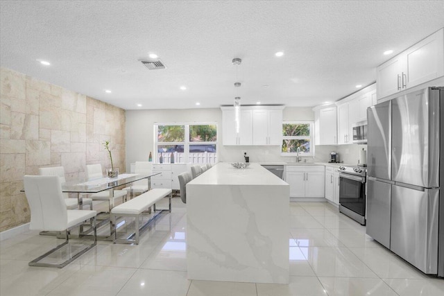 kitchen with light stone countertops, hanging light fixtures, white cabinets, and stainless steel appliances