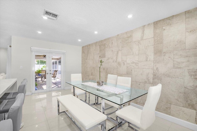 dining area featuring a textured ceiling, light tile patterned floors, tile walls, and french doors