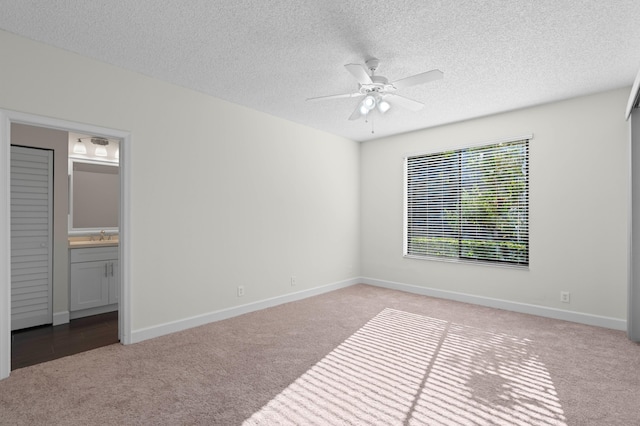 unfurnished bedroom featuring connected bathroom, light carpet, ceiling fan, and a textured ceiling