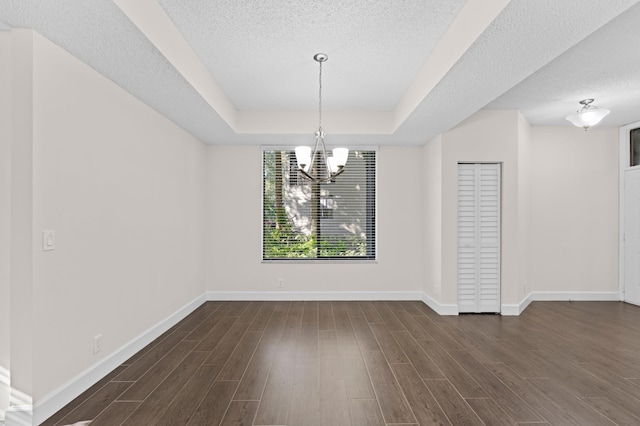 unfurnished dining area with a textured ceiling, a raised ceiling, dark wood-type flooring, and an inviting chandelier