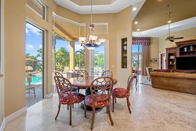 dining space featuring ceiling fan with notable chandelier, a high ceiling, and a tray ceiling