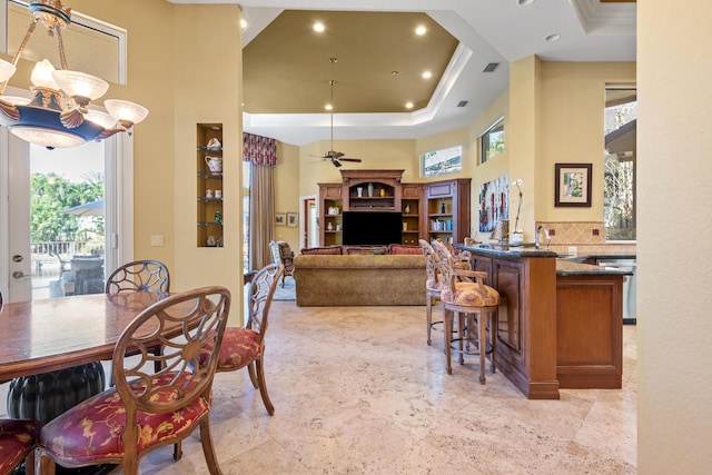 dining room featuring sink, crown molding, a towering ceiling, a tray ceiling, and ceiling fan with notable chandelier