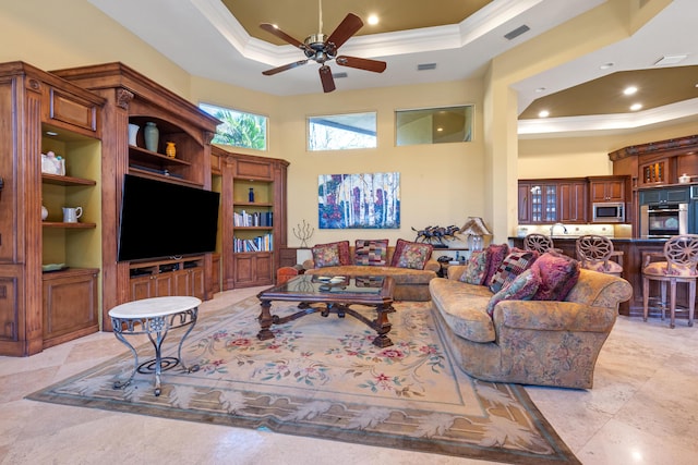 living room with built in shelves, ceiling fan, crown molding, a towering ceiling, and a tray ceiling