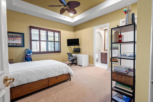 carpeted bedroom featuring a tray ceiling, ensuite bath, and ceiling fan