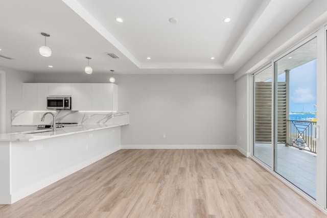 kitchen featuring light wood-type flooring, light stone counters, a raised ceiling, pendant lighting, and white cabinets