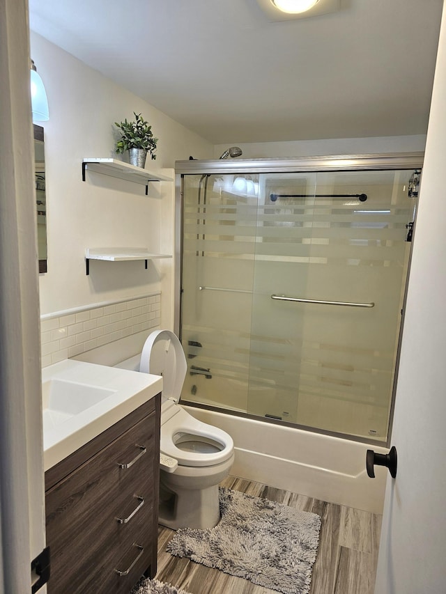 full bathroom with hardwood / wood-style floors, bath / shower combo with glass door, toilet, vanity, and tile walls