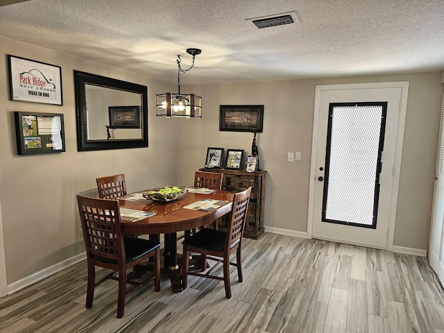 dining space with hardwood / wood-style floors, a notable chandelier, and a textured ceiling