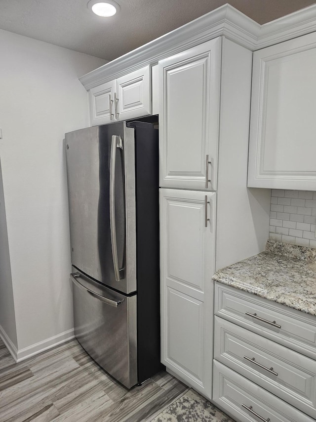 kitchen featuring white cabinets, decorative backsplash, stainless steel fridge, light stone countertops, and light hardwood / wood-style floors