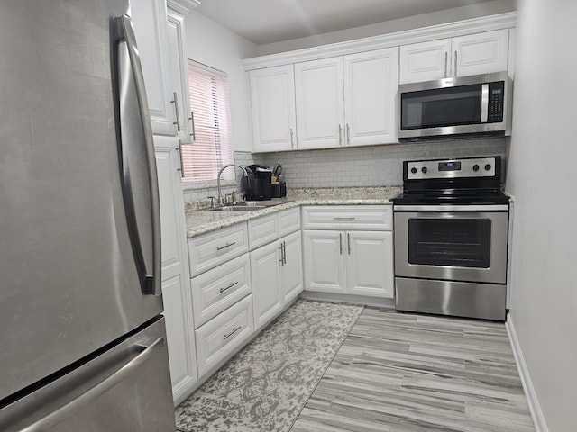 kitchen with decorative backsplash, appliances with stainless steel finishes, light stone counters, sink, and white cabinets