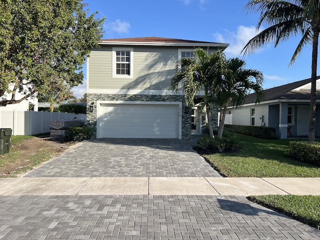 traditional-style house with a garage, stone siding, fence, decorative driveway, and a front yard