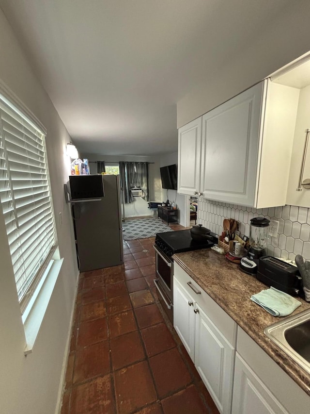 kitchen featuring stainless steel gas stove, sink, fridge, decorative backsplash, and white cabinets