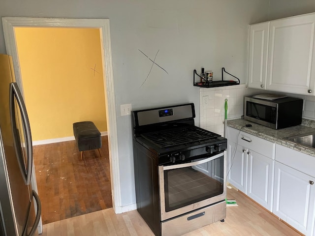 kitchen with white cabinets, appliances with stainless steel finishes, light wood-type flooring, and tasteful backsplash