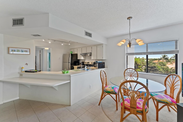 kitchen featuring appliances with stainless steel finishes, light tile patterned floors, white cabinetry, and hanging light fixtures