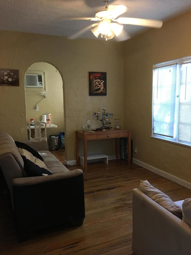 living area with arched walkways, a textured wall, wood finished floors, baseboards, and a wall mounted air conditioner