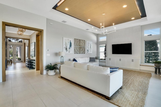 living room featuring a raised ceiling, light tile patterned floors, a high ceiling, and an inviting chandelier