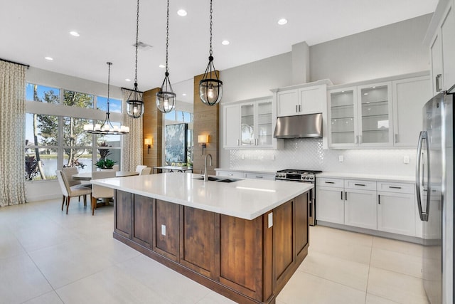 kitchen with sink, hanging light fixtures, a kitchen island with sink, white cabinets, and appliances with stainless steel finishes