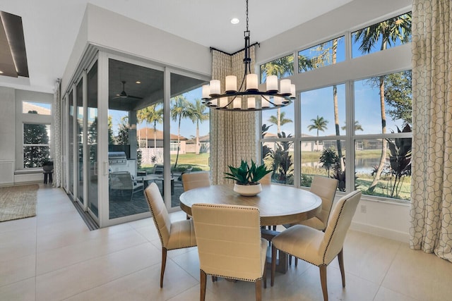 dining room featuring ceiling fan with notable chandelier, a water view, and light tile patterned floors