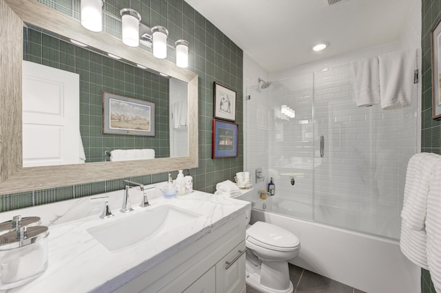 full bathroom with tile walls, shower / bath combination with glass door, vanity, toilet, and tile patterned floors