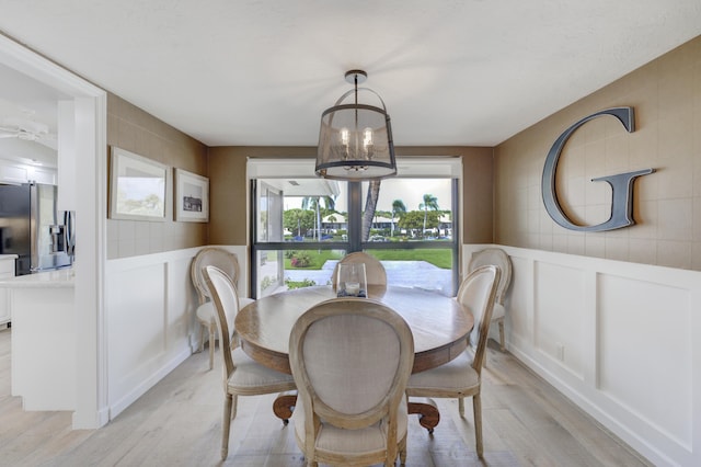 dining space with light wood-style floors, a chandelier, and a decorative wall