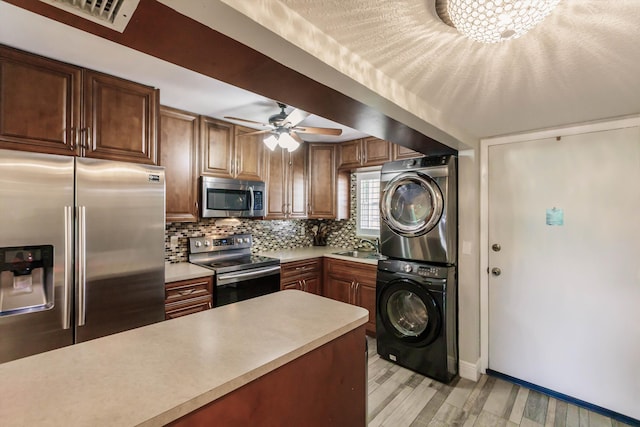 kitchen featuring stacked washer and clothes dryer, backsplash, stainless steel appliances, light wood-style floors, and light countertops