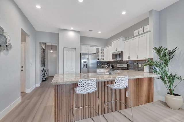 kitchen with white cabinetry, stainless steel appliances, decorative backsplash, light stone countertops, and a breakfast bar