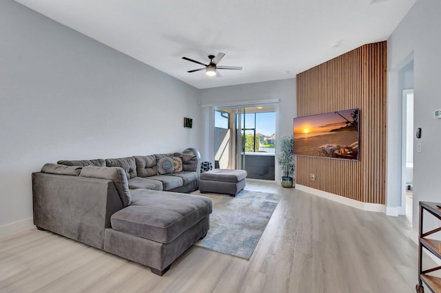 living room featuring ceiling fan, wooden walls, and light hardwood / wood-style floors