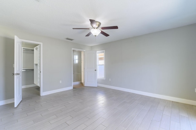 unfurnished bedroom featuring a closet, a spacious closet, ceiling fan, and light hardwood / wood-style floors