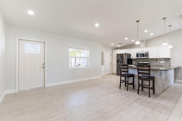 kitchen with white cabinetry, sink, kitchen peninsula, lofted ceiling, and appliances with stainless steel finishes