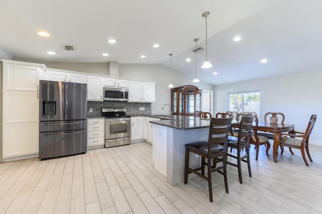 kitchen with decorative backsplash, appliances with stainless steel finishes, dark stone counters, sink, and pendant lighting