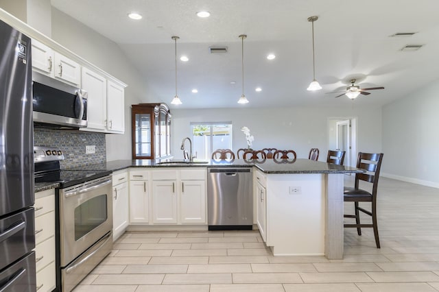 kitchen with white cabinetry, sink, stainless steel appliances, backsplash, and decorative light fixtures