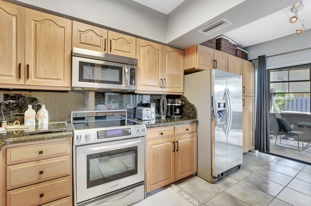 kitchen featuring a kitchen bar, light brown cabinetry, stainless steel dishwasher, a kitchen island, and hanging light fixtures