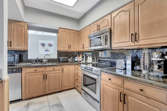 kitchen featuring tasteful backsplash, stainless steel appliances, sink, light tile patterned floors, and dark stone countertops