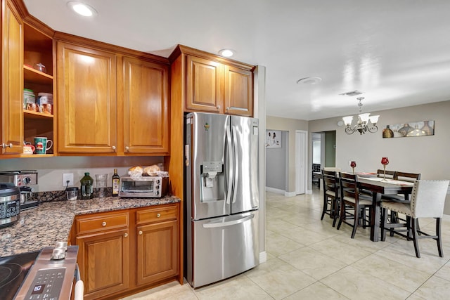 kitchen with stove, dark stone counters, stainless steel refrigerator with ice dispenser, decorative light fixtures, and a chandelier