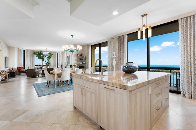 kitchen featuring a wall of windows, a center island with sink, hanging light fixtures, and an inviting chandelier