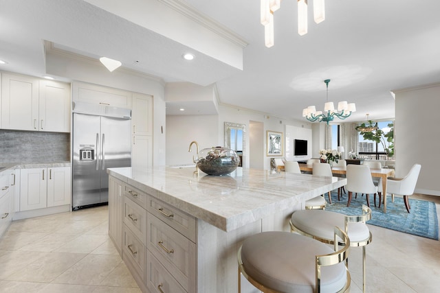 kitchen featuring pendant lighting, crown molding, stainless steel built in fridge, and an island with sink