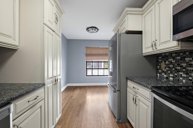 kitchen featuring decorative backsplash, appliances with stainless steel finishes, wood-type flooring, dark stone countertops, and white cabinets