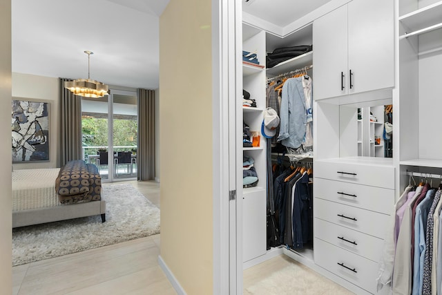 walk in closet with light wood-style floors and a notable chandelier