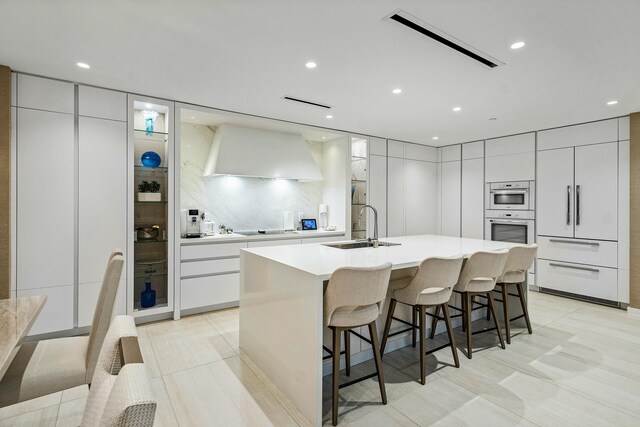 kitchen featuring wall chimney exhaust hood, modern cabinets, visible vents, and a sink