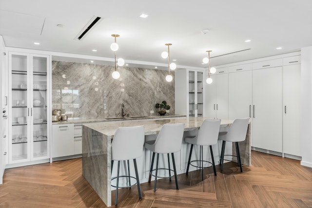 kitchen with sink, white cabinetry, pendant lighting, parquet flooring, and a spacious island