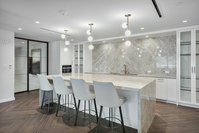 kitchen with hanging light fixtures, oven, modern cabinets, white cabinetry, and a kitchen island