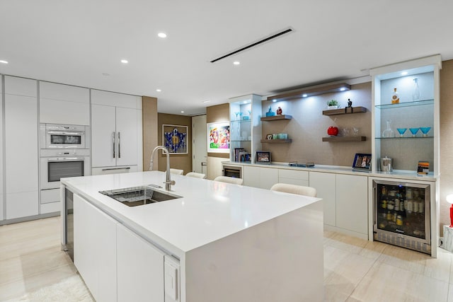 kitchen with a center island with sink, sink, white cabinets, and beverage cooler