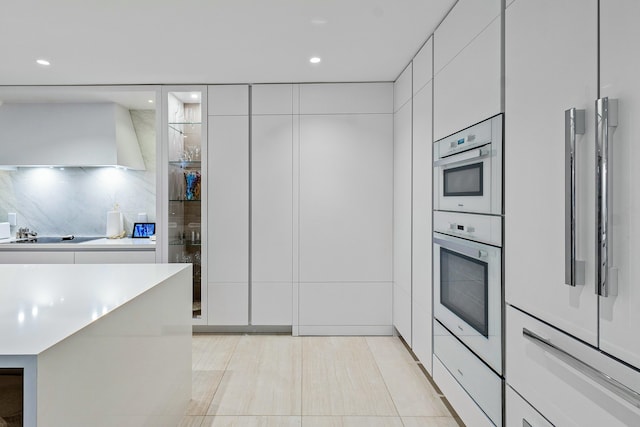 kitchen featuring wall chimney exhaust hood, white cabinets, black electric cooktop, backsplash, and light tile patterned floors