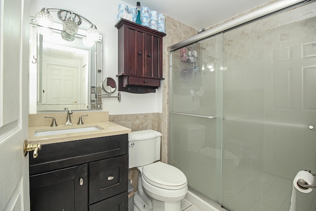 bathroom featuring vanity, toilet, tile walls, and a shower with shower door