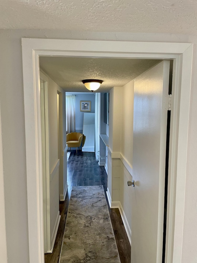 hall with a textured ceiling and dark hardwood / wood-style flooring