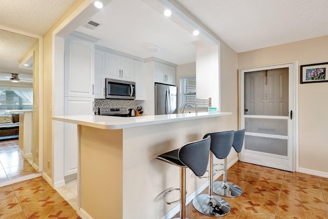 kitchen featuring kitchen peninsula, a kitchen breakfast bar, backsplash, stainless steel appliances, and white cabinets