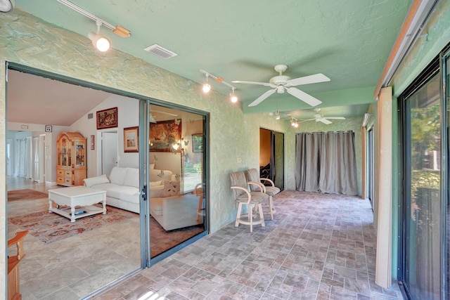 unfurnished sunroom featuring vaulted ceiling, track lighting, and ceiling fan