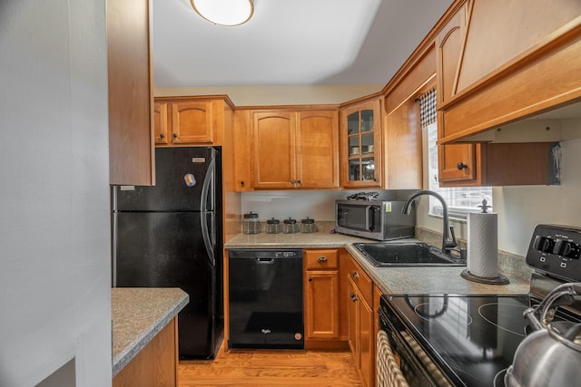 kitchen with premium range hood, black appliances, sink, light wood-type flooring, and light stone counters