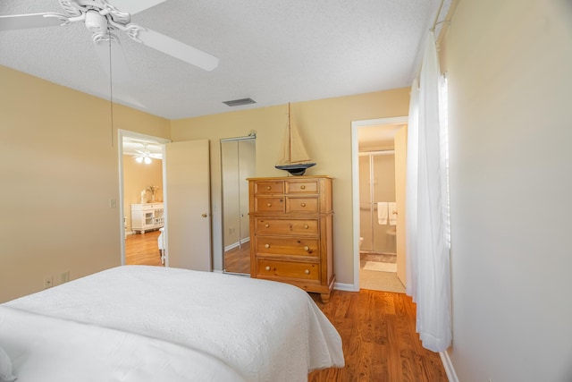 bedroom with a textured ceiling, light hardwood / wood-style floors, ceiling fan, and connected bathroom